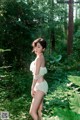 A woman in a white lingerie standing in the woods.