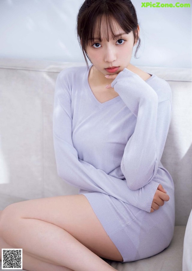 A woman sitting on a white couch wearing a gray sweater dress.