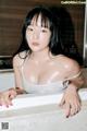 A woman in a white tank top sitting in a bathtub.