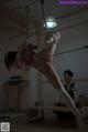 A woman tied up on a rope in a room.
